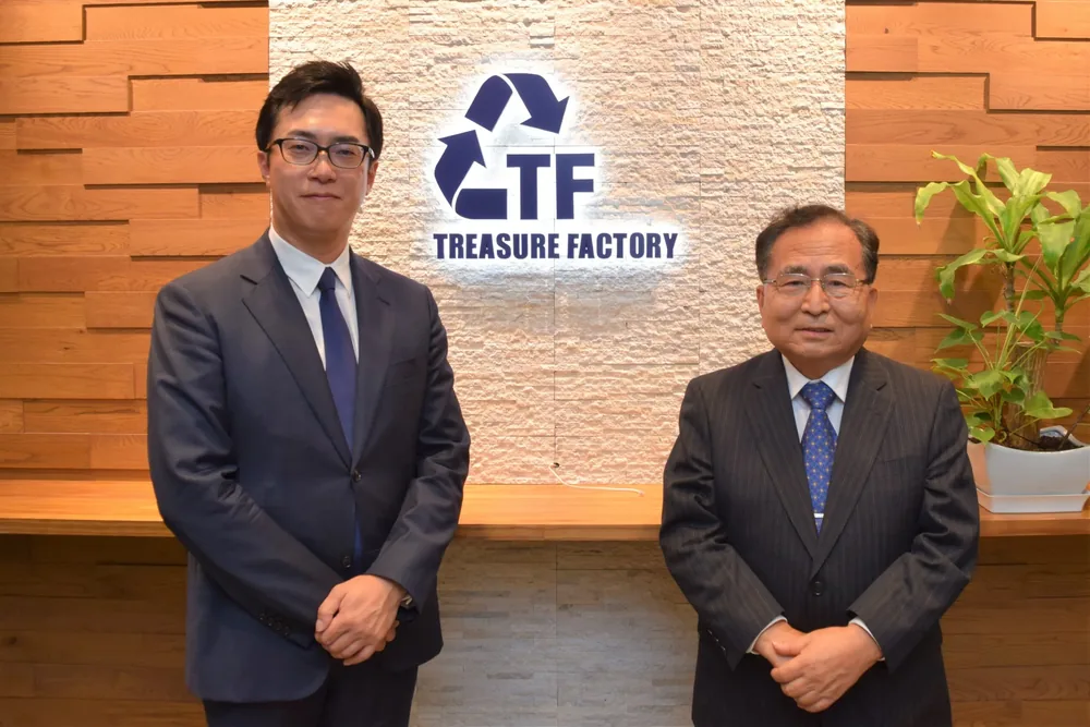 譲受企業のロゴを掲げた壁の前に並ぶ、株式会社トレジャー・ファクトリー 代表取締役社長 野坂英吾様と、株式会社ピックアップジャパン 代表取締役社長 青島克樹様